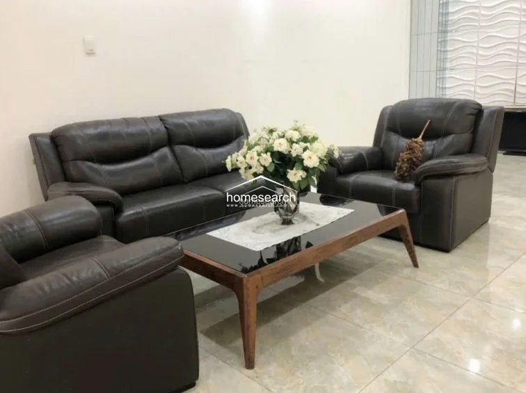 A close-up of the living area highlights the dark leather furniture and a contemporary wooden coffee table with a glass top. The neutral wall finishes and minimalist decor emphasize a clean, well-maintained aesthetic throughout the room.