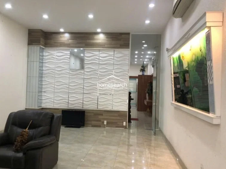 This view showcases a feature wall with white 3D wave-patterned panels and wood-toned accents, providing a sophisticated focal point for the living space. The room is equipped with a wall-mounted air conditioning unit and recessed ceiling lighting, reflecting a high level of maintenance and modern design.