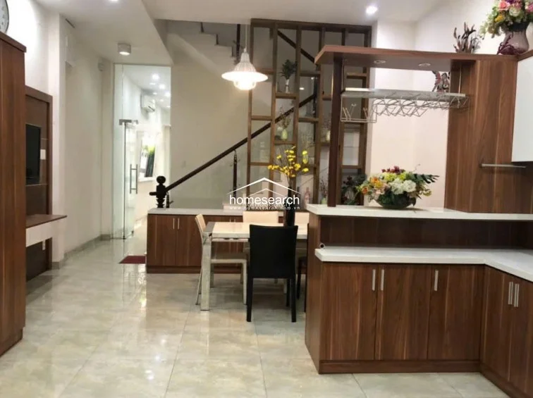 The dining and kitchen area features an efficient, open-concept layout with a wooden dining set and a breakfast bar that separates the kitchen from the rest of the home. Architectural details include a decorative open-shelf partition near the staircase, which adds both storage and visual interest while maintaining an airy, connected flow.