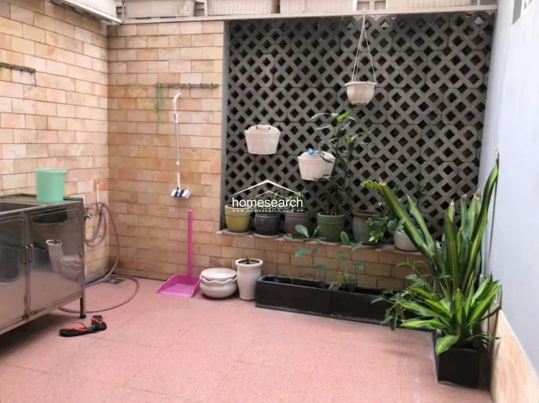 This outdoor patio area serves as a functional utility or garden space, featuring textured stone-tiled flooring and a unique decorative breeze-block wall. It is equipped with a stainless steel utility sink and wall-mounted hooks for storage, making it a practical area for maintenance or gardening. The space is well-maintained and offers a semi-private, airy atmosphere perfect for potted plants and outdoor chores.