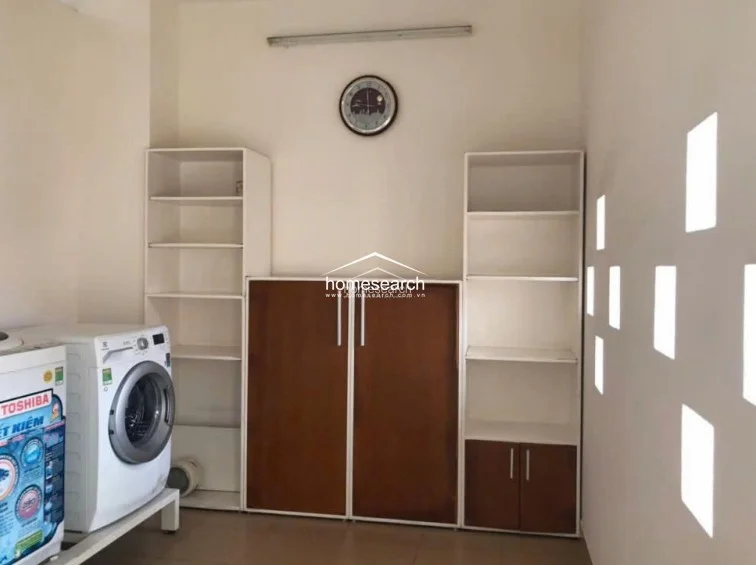This utility or laundry room is efficiently designed with white and wood-toned cabinetry providing ample open and closed storage. A modern front-loading washing machine is neatly integrated into the layout, and the room features distinctive square wall cutouts that add a modern architectural touch. The space is clean and well-organized, with neutral walls and flooring that maintain a consistent, minimalist aesthetic.
