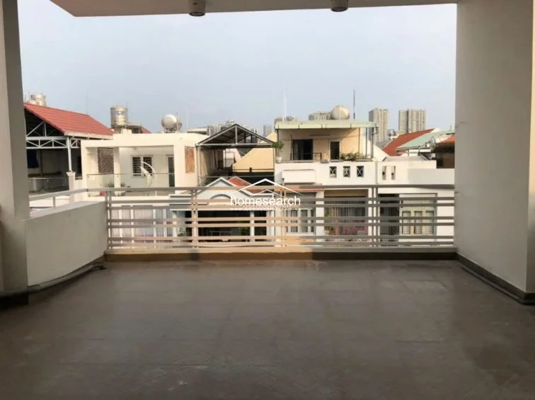 This expansive covered balcony offers a functional outdoor living space with durable tiled flooring and a protective metal railing. It provides an elevated view of the surrounding neighborhood and residential rooftops, offering a private area that is well-maintained and ready for outdoor seating or plants.