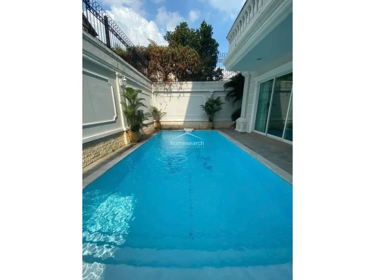 This shot provides a closer look at the swimming pool, emphasizing its clear blue water and the surrounding manicured pool deck. The wall finishes consist of elegant white paneling with classical trim, reflecting a high level of maintenance and a luxurious, resort-like atmosphere.