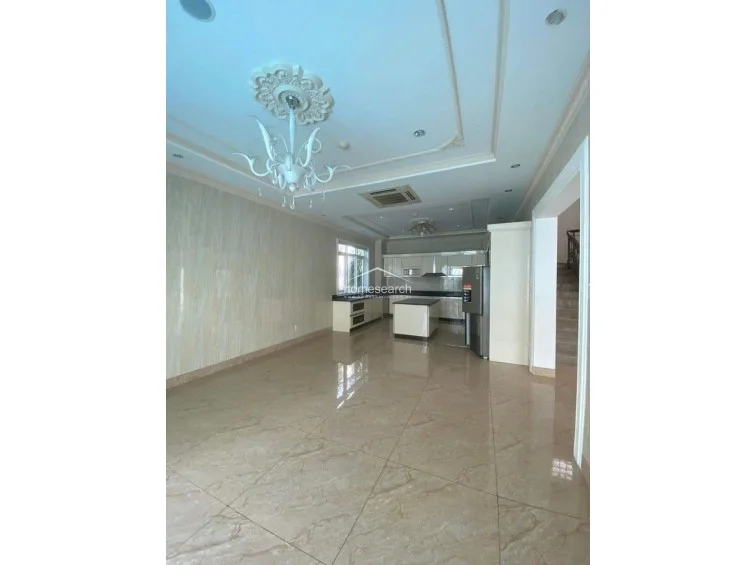 This expansive open-plan kitchen and dining area is designed for functionality and style, featuring a central island and a large, modern refrigerator. The room is bathed in natural light from a large window and is finished with elegant marble flooring and a decorative ceiling medallion, reflecting a high level of maintenance and luxury.