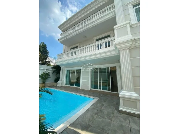 This image focuses on the rear elevation of the villa, showcasing its multi-level balconies with classic balustrade railings and tall, fluted columns. The large sliding glass doors provide direct access to the pool area, highlighting the property's emphasis on natural light and integrated living spaces.