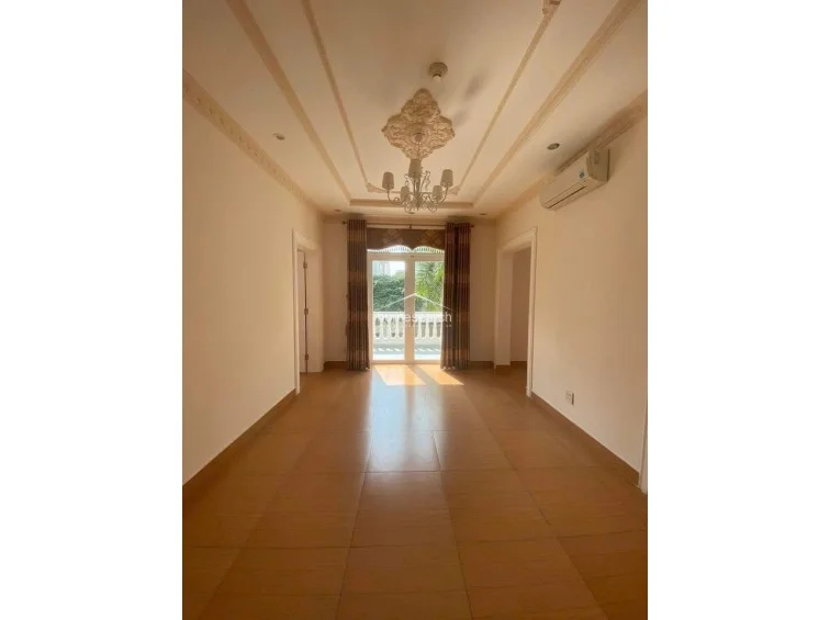 This bright, airy living space features an open-plan layout that leads directly to an outdoor balcony through glass doors. The room is accented by sophisticated ceiling detailing, recessed lighting, and a central chandelier, all set against a neutral color palette and consistent tile flooring.