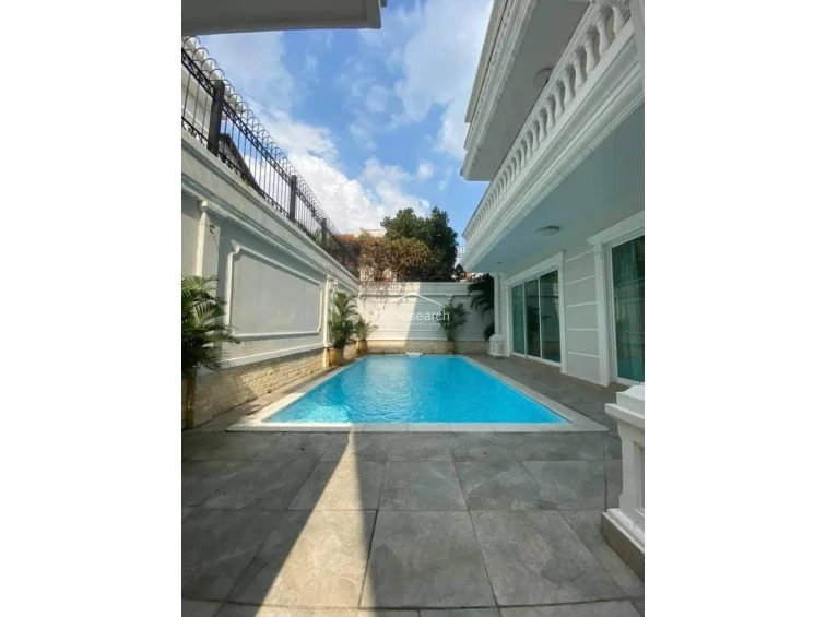 This view highlights a private outdoor swimming pool area situated directly adjacent to the villa, creating a seamless indoor-outdoor flow through large sliding glass doors. The space is enclosed by high, decorative walls for privacy and features grey stone decking, potted greenery, and a clean, modern aesthetic.