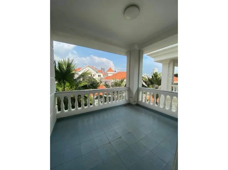 This covered balcony offers a generous outdoor living space with classic balustrade railings and blue tile flooring. It provides a pleasant view of the surrounding neighborhood and lush greenery, serving as a peaceful extension of the interior living areas.