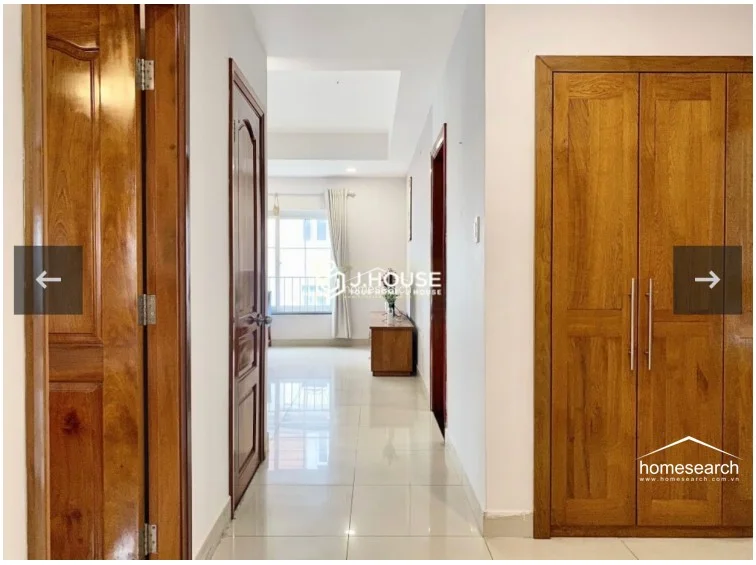 A hallway connects the main living area to other parts of the home, featuring high-quality wooden doors and a large, built-in wooden wardrobe for ample storage. The space maintains a consistent aesthetic with light-colored tile floors and clean, white-painted walls, suggesting a well-maintained interior.
