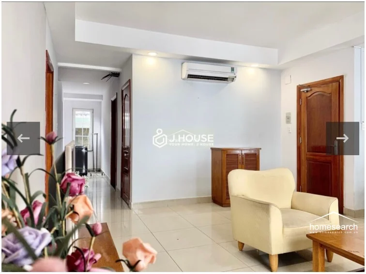 This view highlights the transition between the living room and the hallway, showing a wall-mounted air conditioning unit for climate control. The area is furnished with a small wooden storage cabinet and maintains the consistent light tile flooring and neutral color palette seen throughout the property.