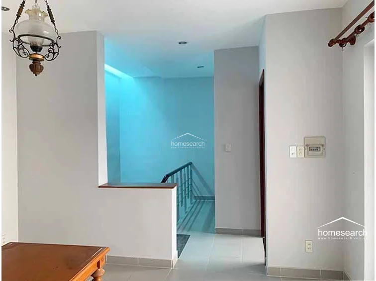 This landing area features a neutral color palette and tiled flooring, connecting the staircase to the rest of the upper level. It is accented by a traditional-style hanging light fixture and offers an open, airy flow with a low partition wall overlooking the stairwell.