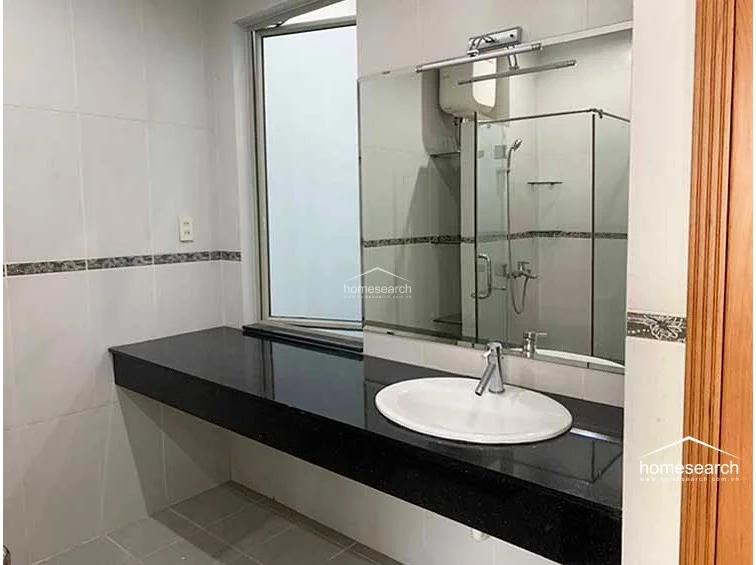 The bathroom is equipped with a sleek black granite vanity countertop and a modern white oval sink. It features full-height wall tiling, a large vanity mirror, and a glass-enclosed shower area, maintaining a functional and well-kept appearance.