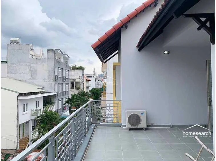 This spacious outdoor terrace offers an expansive view of the surrounding urban neighborhood and is finished with durable grey floor tiles. The area is partially covered by a pitched roof with terracotta tiles and includes an exterior AC unit, providing a versatile space for outdoor relaxation.