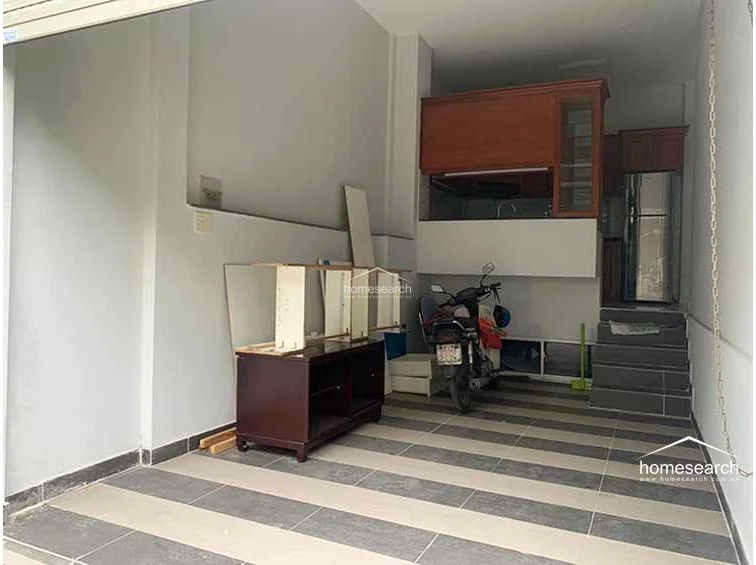 This ground-floor space serves as a functional garage or utility area, featuring durable, modern striped floor tiles. It includes a raised platform area with wooden cabinetry and a refrigerator, providing a seamless transition between storage and living utility.