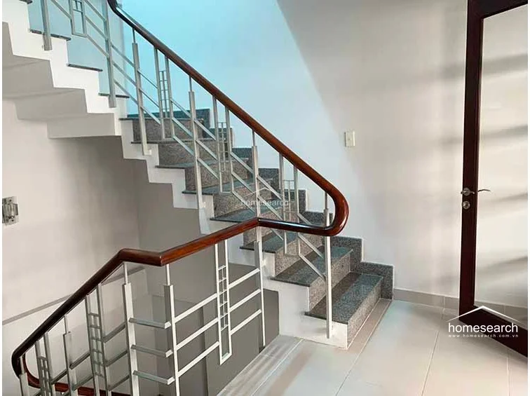 This staircase features a sturdy metal railing with a polished wooden handrail, leading to an upper level with a clear view of the landing. The steps are finished in a durable, speckled stone material, contrasting nicely with the clean white walls and neutral tile flooring of the hallway.