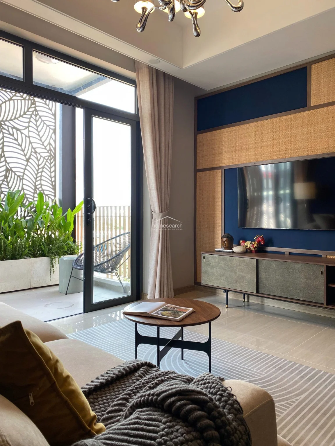 The living area is centered around a circular wooden coffee table and a textured area rug, creating a warm and inviting atmosphere. The design emphasizes architectural detail through the use of mixed materials like rattan and wood, all while maintaining an unobstructed view of the outdoor terrace.