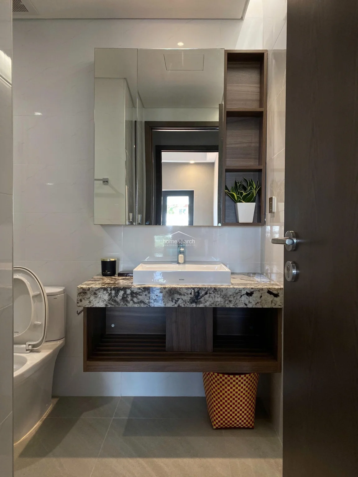 This vanity area showcases a modern floating cabinet with a granite countertop and a vessel sink, paired with an integrated mirror and open shelving for storage. The space is finished with clean, white wall tiles and dark wood accents, creating a sharp, high-contrast look. It is well-maintained and efficiently designed to maximize storage without sacrificing style.