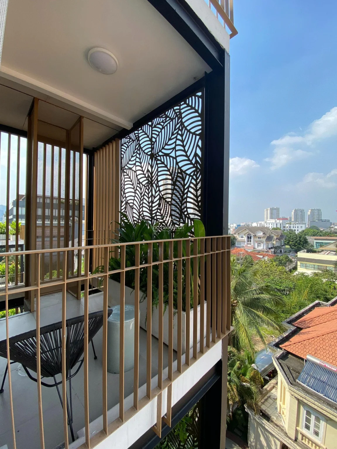 The balcony offers an elevated perspective of the surrounding neighborhood, featuring a unique laser-cut leaf-patterned privacy screen that adds both style and shade. The space is well-maintained, equipped with a modern chair and built-in planters, making it an ideal spot for outdoor relaxation.