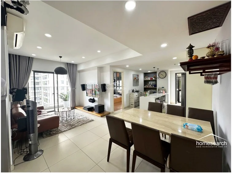 This open-concept living and dining area features a modern, neutral color palette with large-format light-colored floor tiles that enhance the sense of space. The layout flows seamlessly from the dining area into a contemporary kitchen, with a balcony accessible through floor-to-ceiling glass doors that provide ample natural light and city views.