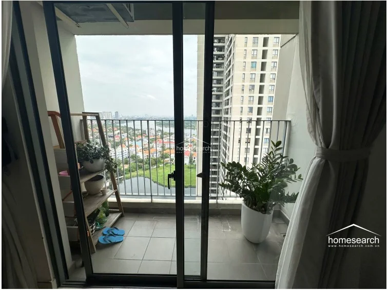 The balcony offers a scenic, elevated view of the surrounding urban landscape and nearby water features, providing a small outdoor retreat. It is finished with durable grey floor tiles and features a metal railing, currently utilized for potted plants and light storage.