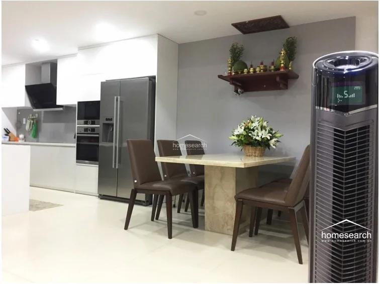 This dining corner highlights a marble-topped table with dark leather chairs, set against a light grey wall adorned with a traditional wooden altar shelf. The area is climate-controlled with a tower fan and maintains a neat, well-kept appearance consistent with the rest of the home.