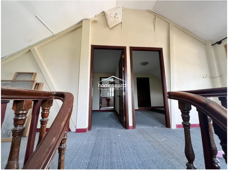 This landing area features a vaulted ceiling with visible signs of water damage and peeling paint, indicating a need for maintenance. The space connects to two separate rooms via dark wood doors and is floored with grey carpeting, showing a dated aesthetic.
