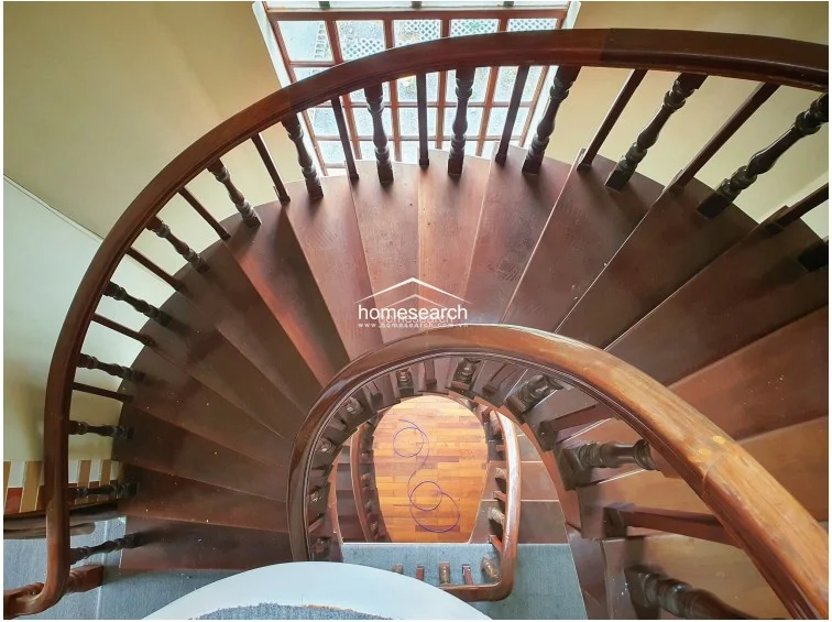 This image captures a classic wooden spiral staircase from a top-down perspective, showcasing the rich, dark timber finish of the steps and railing. The design creates a strong architectural focal point, though the surrounding area appears to be in a state of transition or light maintenance.