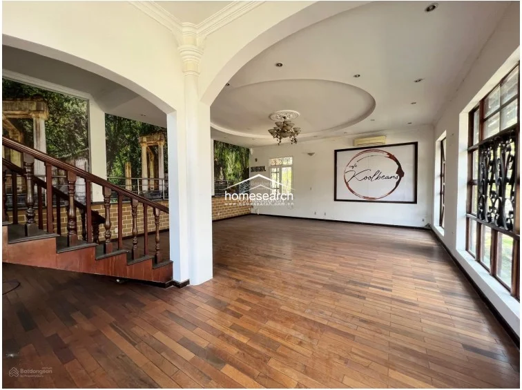 This expansive, open-plan living area is defined by polished hardwood floors, grand arched architectural details, and a prominent white column. The space is flooded with natural light from large windows and features decorative wall murals, suggesting a versatile area previously used for both residential and commercial purposes.