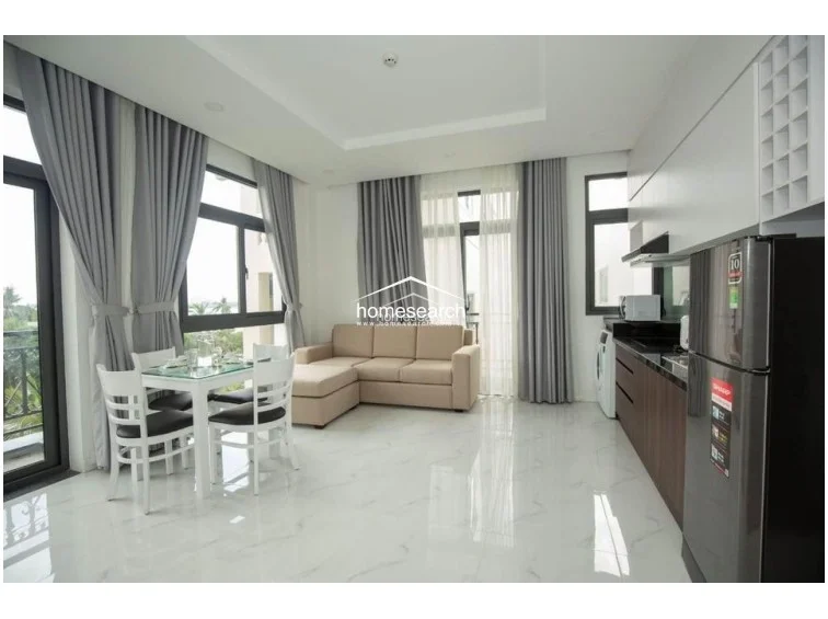 This open-concept living and dining area features polished white marble-style tile flooring and a modern, minimalist aesthetic. Large floor-to-ceiling windows with grey floor-length curtains provide ample natural light and a scenic outdoor view, while the kitchen is equipped with dark wood cabinetry, a black countertop, and a full-sized refrigerator.
