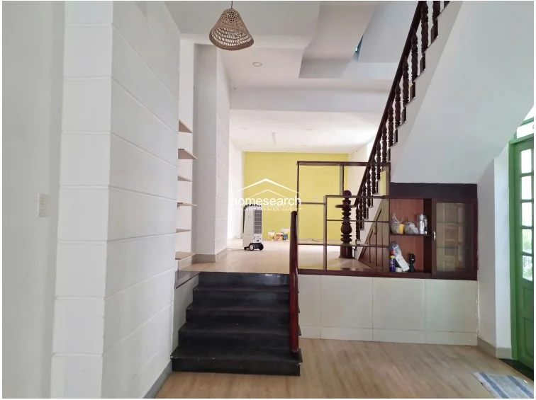 This view focuses on the staircase area, which features dark stone steps and a traditional dark wood balustrade with ornate carved details. Built-in under-stair storage and open wall-mounted shelving provide functional organization, while the rear section of the room is finished with a contrasting yellow accent wall.