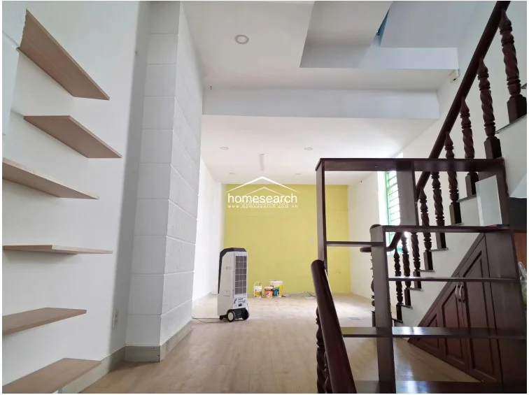 A closer look at the staircase and shelving area reveals the contrast between the light wood flooring and the dark wood cabinetry and stair structure. The space is well-maintained, featuring recessed lighting and a clean, neutral color palette that highlights the architectural transition between the front and rear sections of the home.