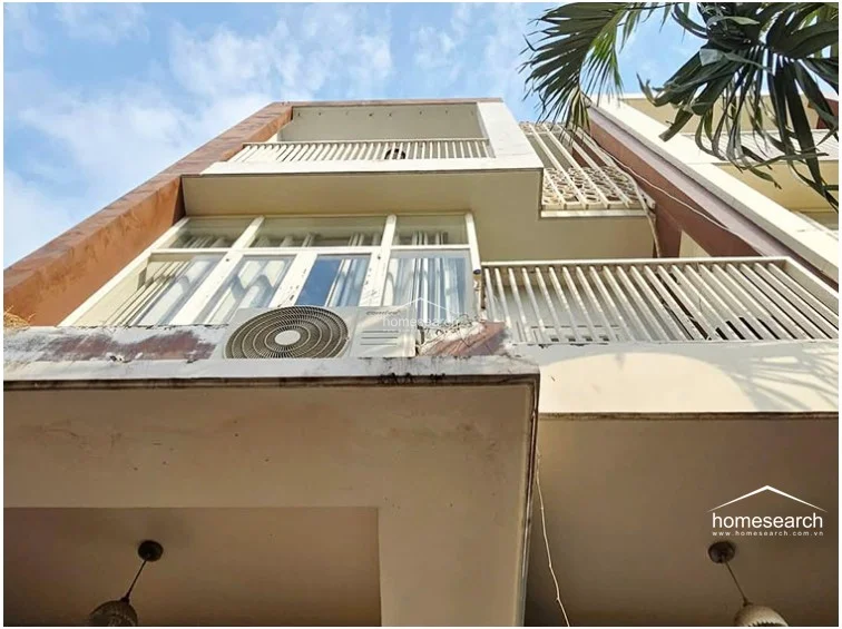 This upward-facing exterior shot highlights the building's multi-level balcony design, which incorporates metal railings and decorative lattice screens. An external AC unit is mounted on the facade, and the structure shows signs of weathering that may require maintenance.