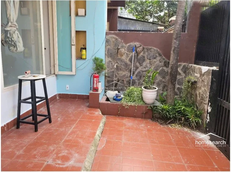 This outdoor patio area features terracotta-style floor tiles and a decorative stone-clad feature wall, creating a rustic transition space. It includes a small built-in planter and serves as a functional exterior zone, though it currently shows signs of clutter and requires some maintenance.