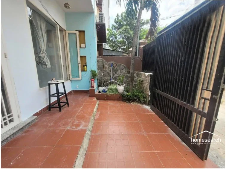This outdoor patio area features terracotta-style floor tiles and a stone-accented wall with a small built-in planter. It is enclosed by a tall, dark metal gate and provides a semi-private transition space leading into the interior via glass doors.