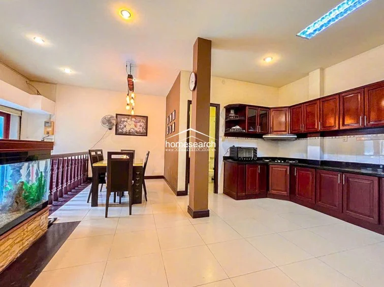 This open-concept dining and kitchen area features light-colored tile flooring and a warm, neutral color palette that enhances the sense of space. The kitchen is equipped with extensive dark wood cabinetry and black countertops, while a large aquarium serves as a unique room divider near the dining set.