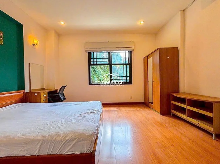 This bedroom layout is identical to the previous one, featuring the same green accent wall, wood-look flooring, and wooden wardrobe. It is furnished with a double bed, a vanity desk, and an additional low-profile wooden storage unit, maintaining a consistent and orderly aesthetic throughout the home.