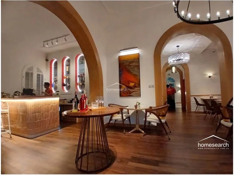 This sophisticated interior space features a bar area with warm under-counter lighting and distinctive arched wall niches for display. The room is characterized by rich wooden flooring, grand arched doorways, and elegant chandeliers, reflecting a high level of maintenance and a luxurious, classic design aesthetic.