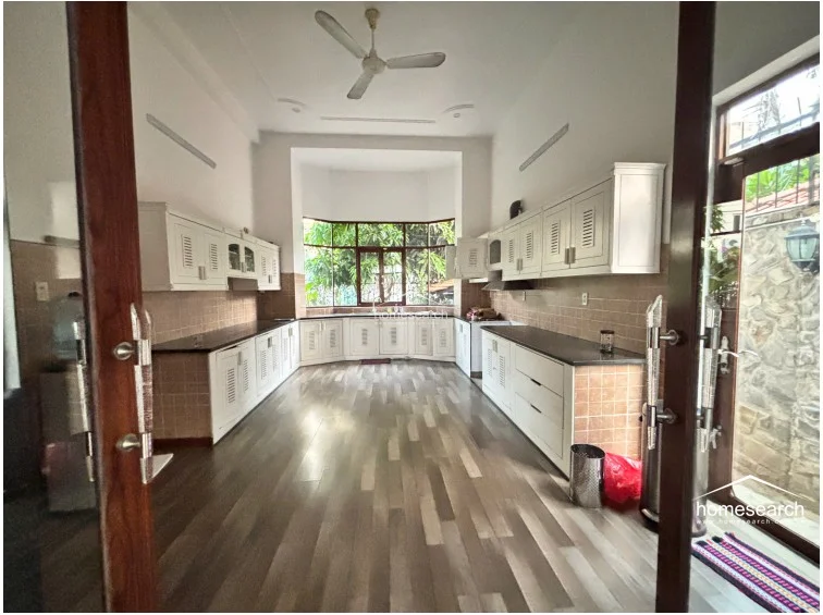 This large, U-shaped kitchen features extensive white cabinetry with louvered details and dark countertops, offering significant storage and workspace. The room is anchored by a unique bay window design that floods the area with natural light, complemented by wood-look flooring and tiled backsplashes.