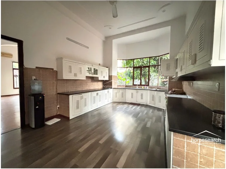This spacious kitchen features a U-shaped layout with white cabinetry providing ample storage and dark countertops for contrast. The room is brightened by a large bay window overlooking greenery and is finished with wood-look flooring and tiled walls, creating a clean, functional environment.