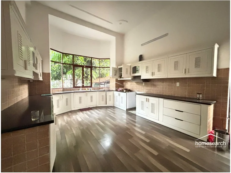 This view of the kitchen emphasizes the generous amount of cabinetry and the functional, spacious layout suitable for a large household. The room maintains a clean, well-maintained aesthetic with a neutral color palette and large windows that provide a pleasant, leafy outlook.