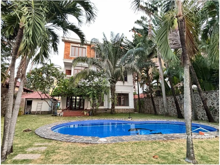 This wide-angle view shows the rear elevation of the three-story villa, which combines white stucco walls with exposed brick detailing on the top level. The property features a seamless flow between the indoor living areas and the outdoor pool deck, showcasing a high level of architectural character and exterior maintenance.