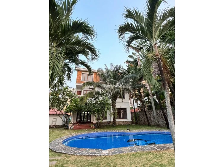 This vertical perspective emphasizes the height and scale of the villa, framed by towering palm trees that create a resort-like atmosphere. The combination of the blue pool, green lawn, and the multi-story structure suggests a luxury residence with significant outdoor amenities and established landscaping.