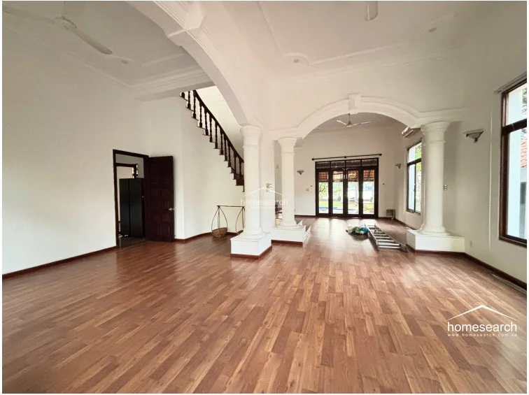 The interior features an open-concept living area defined by elegant architectural details, including grand white columns and arched transitions. Warm wood-look flooring contrasts beautifully with the crisp white walls, while large glass doors provide abundant natural light and direct access to the garden.