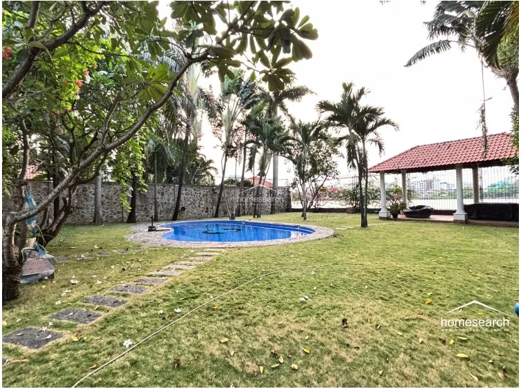 This perspective emphasizes the generous size of the garden and the seamless transition between the pool area and the covered outdoor pavilion. The stone-paved walkway leads through the well-maintained grass, offering a peaceful and private backyard retreat.