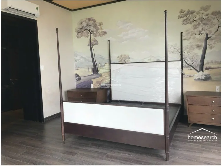 This bedroom features a sophisticated four-poster bed as the focal point, complemented by matching wooden nightstands and a large-scale landscape mural on the main wall. The room is finished with dark wood-style flooring and includes a wall-mounted AC unit, reflecting a well-maintained and elegant aesthetic.