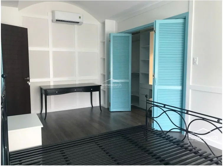 This bedroom showcases a unique architectural vaulted ceiling and bright, white paneled walls that create a clean, airy atmosphere. It includes a dark wood desk, a minimalist black metal bed frame, and vibrant light-blue louvered doors that open into a spacious walk-in wardrobe.