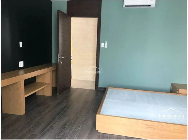 This bedroom features a calming sage green wall color contrasted by a bold black accent wall and dark wood-look flooring. It includes a custom-built wooden bed frame and a matching desk unit, with a wall-mounted AC unit for climate control.
