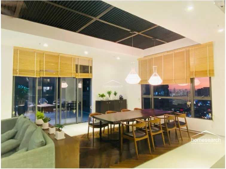 This elegant dining area is defined by a deep-toned herringbone wood floor and a matching dark wood-slatted ceiling feature. It is illuminated by modern pendant lighting and offers expansive city views through large windows, seamlessly flowing into an outdoor terrace space.