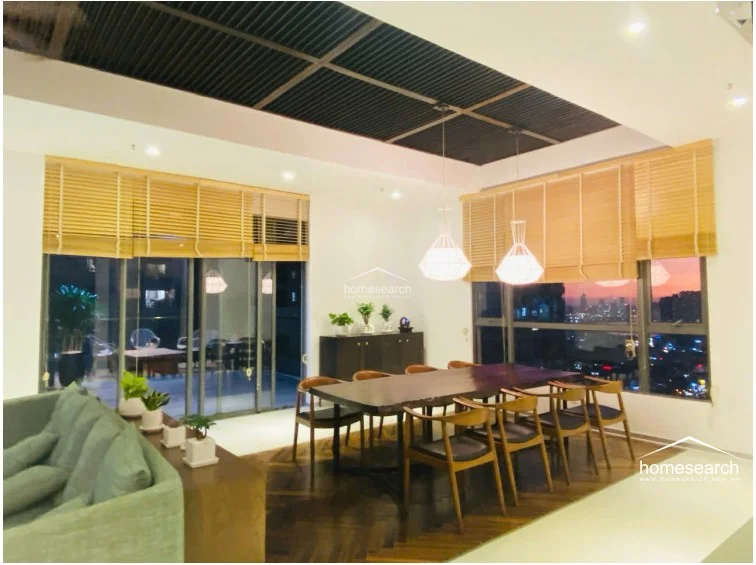 The dining area is defined by a sophisticated herringbone wood floor and a unique slatted ceiling design with modern geometric pendant lights. It flows seamlessly into the living space and features large windows with bamboo blinds that offer an expansive city view.