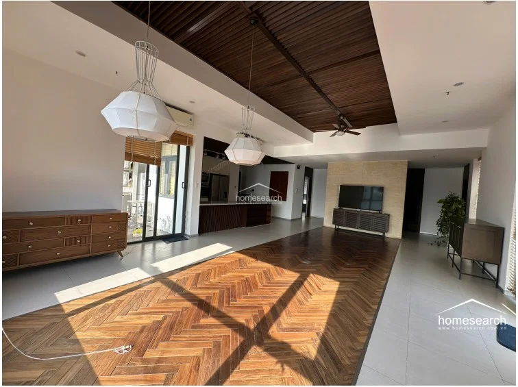 This spacious open-plan living and dining area is anchored by a stunning herringbone wood floor and a dark slatted ceiling feature. The layout is bright and airy, connecting to a balcony through sliding glass doors, and includes high-quality wooden furniture and integrated lighting.